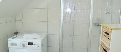 Un baño pequeño con lavadora, cabina de ducha y un armario de madera.