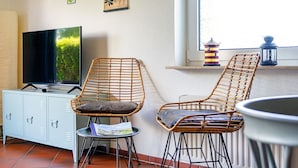 Ein Zimmer mit Fernseher, Korbstühlen, einem kleinen Tisch, einem Schrank und einem Fenster mit Ausblick.