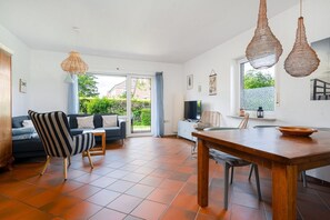 Een ruime woonkamer met een bank, gestreepte fauteuil en een eettafel.