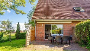 Ein Haus mit Ziegeldach, Backsteinfassade und einer Terrasse mit Tisch und Stühlen.