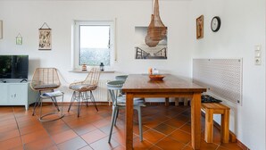 Eine moderne Küche mit einem Holztisch, zwei Korbstühlen, einer Hängelampe und einem Fenster mit Ausblick.