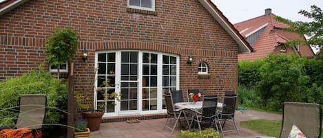 Ein Ziegelhaus mit Terrasse, einem Esstisch und Gartenstühlen.