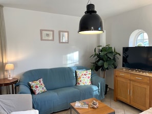 Una sala de estar con un sofá azul, un mueble de madera, un televisor y una planta grande.