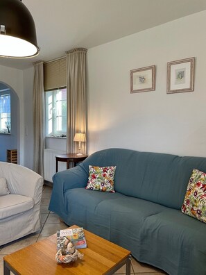 Un salon comprenant un canapé, un fauteuil et une table basse. Deux tableaux encadrés ornent le mur, et une lampe est posée sur une table d’appoint.