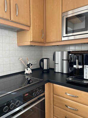 Una cocina moderna con armarios de madera, un microondas de acero inoxidable, una cafetera y una cocina de inducción negra.