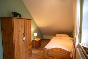 Un dormitorio con techo inclinado, un armario de madera, una mesita de noche con lámpara y una cama con edredón blanco.