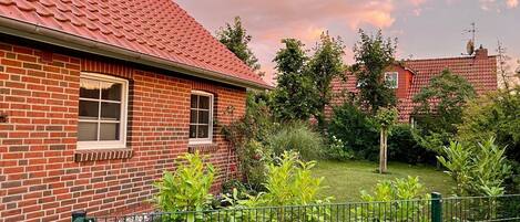 Ein Backsteinhaus mit rotem Ziegeldach, ein kleiner Garten mit Grünpflanzen und ein grüner Metallzaun.