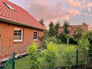 A brick house with a red tiled roof, a small garden with green plants, and a green metal fence.