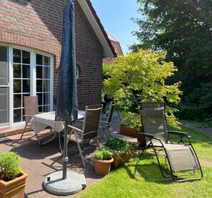 Eine Terrasse mit Tisch, Stühlen, Sonnenschirm und Blumentöpfen.