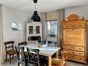 A dining area with a white table, black chairs, a wooden cabinet, and a window with curtains.