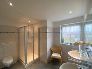 Ein Badezimmer mit Duschkabine, Toilette, Waschbecken mit Spiegel und einem Fenster mit Vorhängen.
