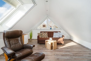 A high-ceilinged room with a sloped ceiling, a brown leather chair, a brown sofa, and a small wooden table. - Mühlenkieker - Cozy vacation apartment (80sqm) for 4 persons with balcony in (Krummhörn)