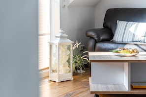 Un salon moderne avec un canapé en cuir, une table blanche sur laquelle se trouve une assiette de nourriture, une lanterne blanche et une plante en pot.