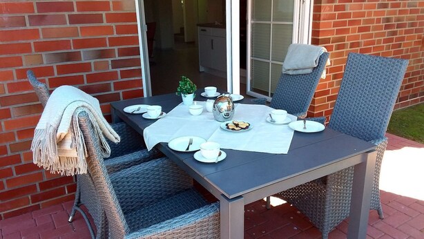 Een eettafel voor vier personen, compleet met rieten stoelen, een wit tafelkleed en een kleine plant in pot.