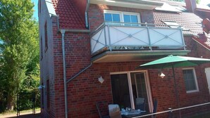 Een tweelaags bakstenen huis met een balkon, een overdekte patio en een zichtbare garageklep.