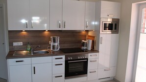 Een moderne keuken met witte kasten, een inbouwoven, een magnetron en een koffiezetapparaat.