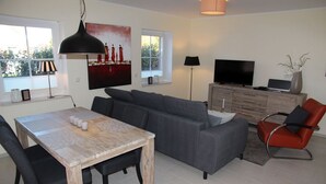 Een moderne woonkamer met een grijze bank, een houten eettafel en een rode stoel.