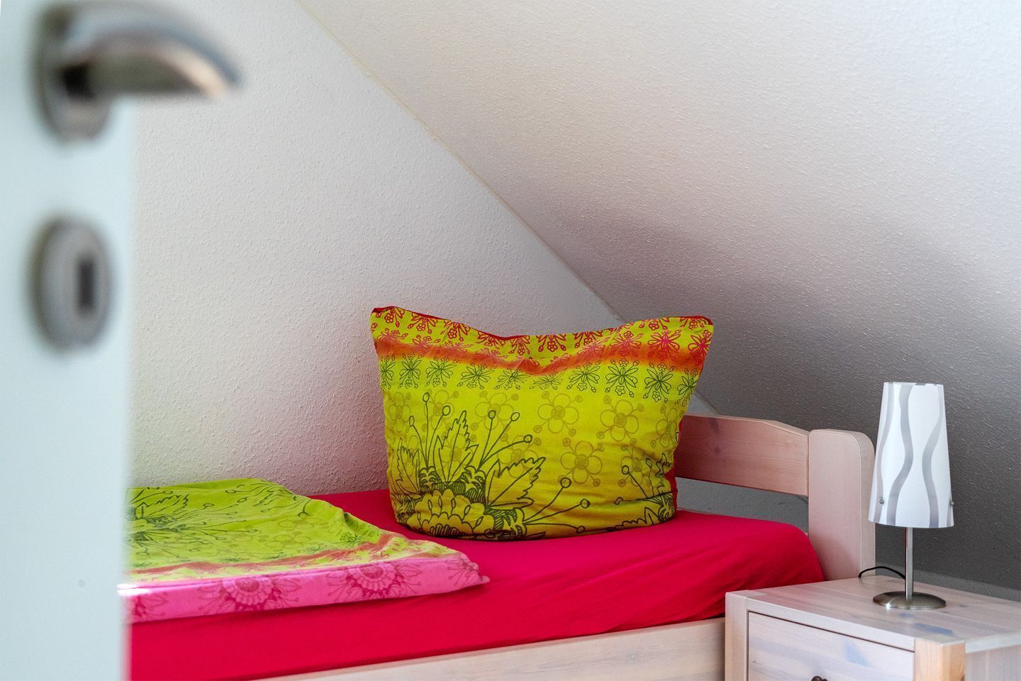 Una camera da letto con un letto, cuscini, un comodino e una lampada.