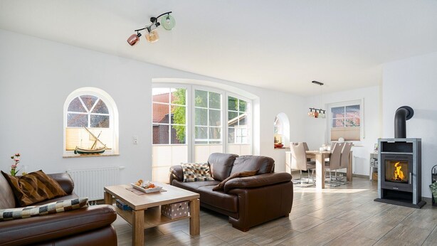 A modern living room with a fireplace, leather sofas, a wooden coffee table, and large windows. - Midsummer - Beautiful vacation home (100sqm) for 6 people with fireplace, garden and (Krummhörn)