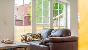A living room with a brown leather sofa, a wooden coffee table, and a window with blinds. - Midsummer - Beautiful vacation home (100sqm) for 6 people with fireplace, garden and (Krummhörn)