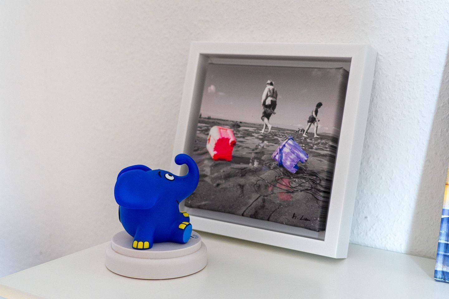 A framed photograph of a beach scene with a blue elephant figurine in front.