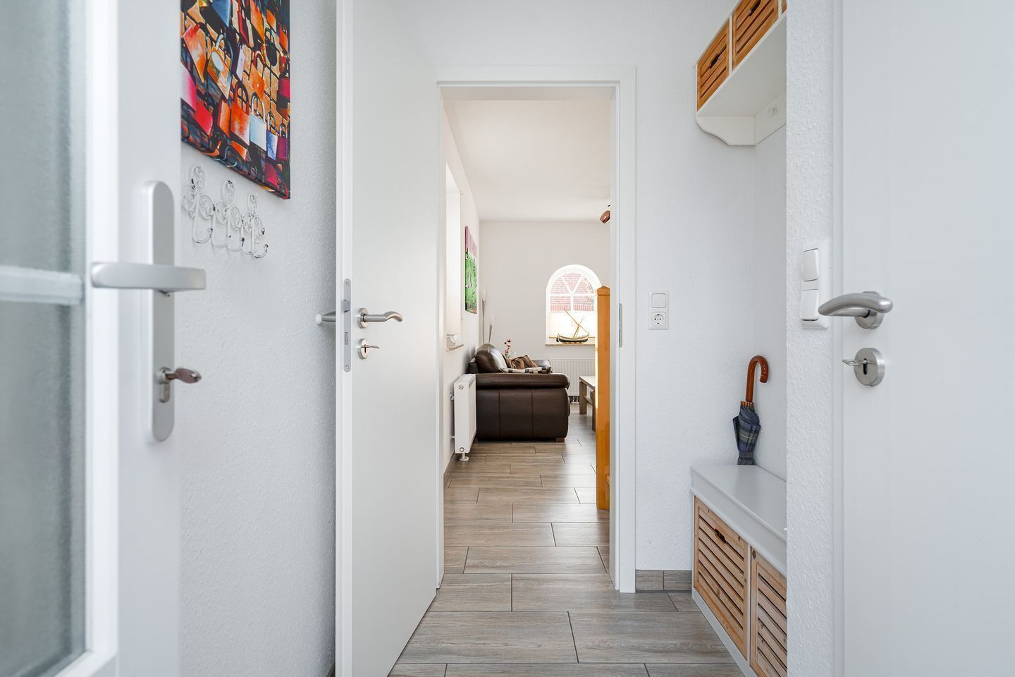 A hallway with a white door, a coat rack, and a painting on the wall.