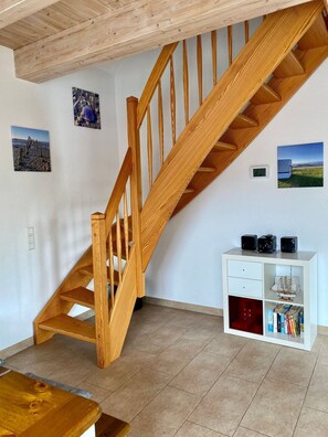 Un escalier en bois dans une pièce où se trouvent un meuble blanc et une petite table.