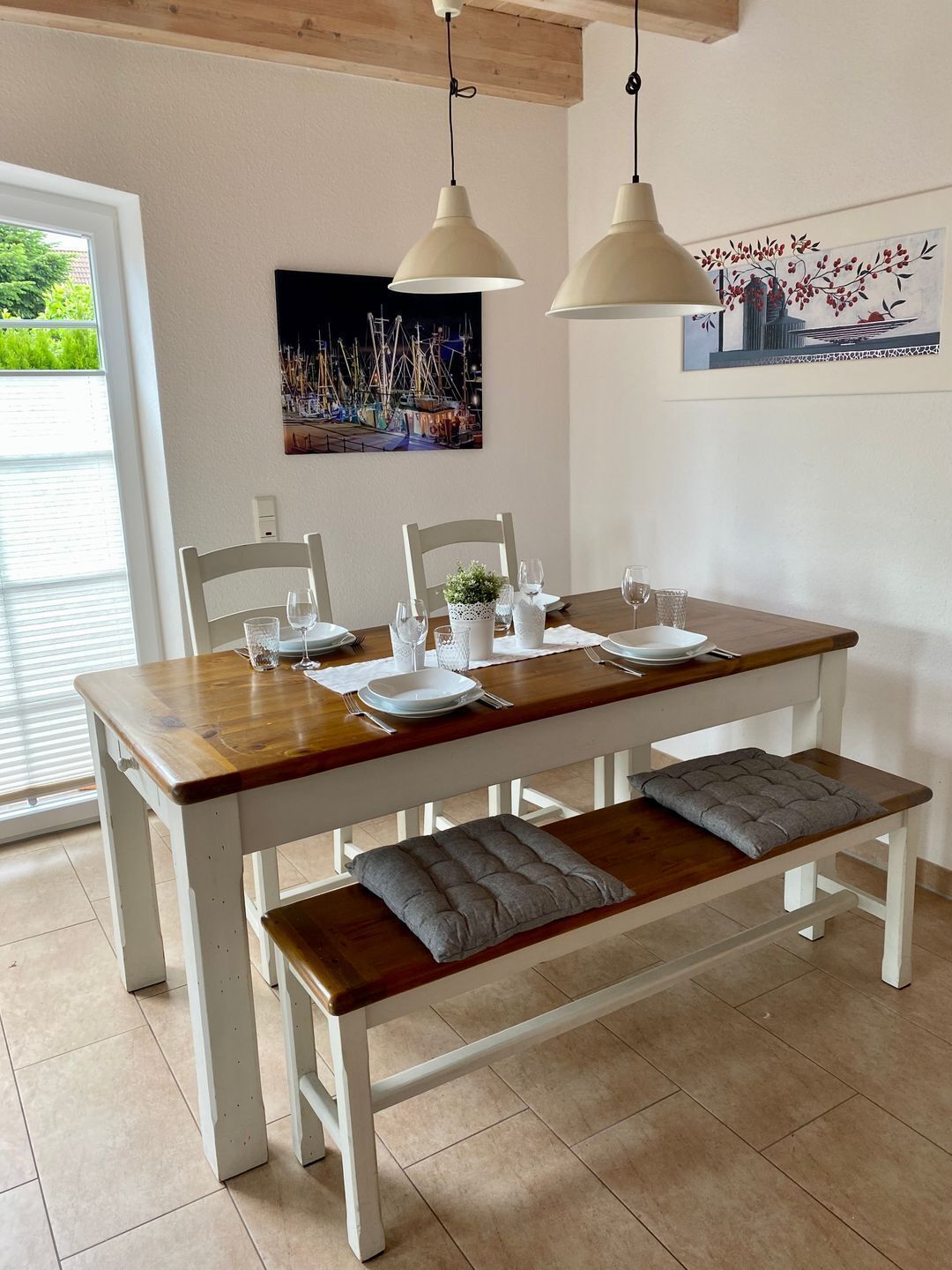 A dining table set with plates, glasses, and cutlery, with a bench and cushions underneath.