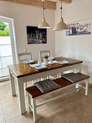 Une table à manger dressée avec des assiettes, des verres et des couverts, avec un banc et des coussins placés en dessous.