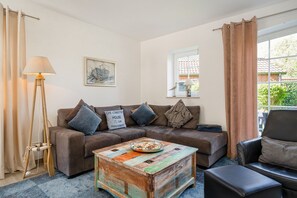 Una sala de estar con un sofá, una mesa de centro, una lámpara y una ventana con cortinas.