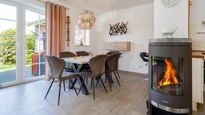 A dining area with a table, chairs, and a modern stove with a visible fire. - Fischhuus - Beautiful vacation home near the water (Krummhörn)