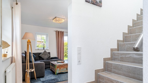A staircase leading to a second floor, a living room with a sofa, a lamp, and a window. - Fischhuus - Beautiful vacation home near the water (Krummhörn)
