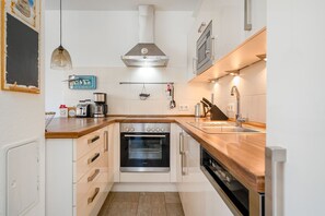 A compact kitchen with a built-in oven, a microwave, and a sink. - Fischhuus - Beautiful vacation home near the water (Krummhörn)