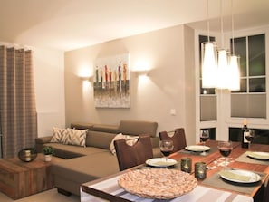 Uma sala de estar com sofá, uma mesa de jantar posta para dois e um quadro na parede.