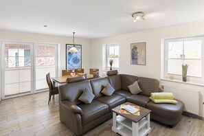 A living room with a brown leather sofa, a coffee table, and a dining area with a table and chairs. - Udo - Schöne Ferienwohnung in Zentraler Lage (Krummhörn)