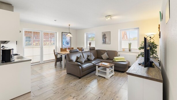 A modern living room with a sofa, coffee table, and a TV on a stand. - Udo - Schöne Ferienwohnung in Zentraler Lage (Krummhörn)