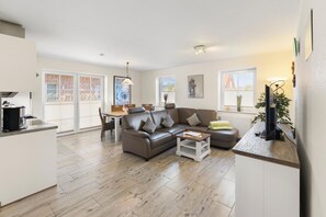 A modern living room with a sofa, coffee table, and a TV on a stand. - Udo - Schöne Ferienwohnung in Zentraler Lage (Krummhörn)
