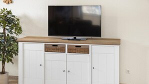 A white cabinet with a wooden top, a flat-screen TV mounted above it, and two wicker baskets on the cabinet doors. - Udo - Schöne Ferienwohnung in Zentraler Lage (Krummhörn)