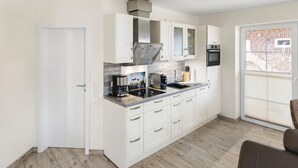 A compact kitchen with white cabinetry, a built-in oven, and a window with a view of a brick building. - Udo - Schöne Ferienwohnung in Zentraler Lage (Krummhörn)