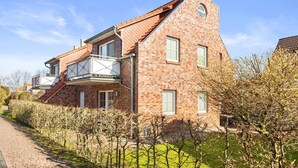 A two-story house with a brick facade, a balcony, and a small tower-like structure on the right side. - Udo - Schöne Ferienwohnung in Zentraler Lage (Krummhörn)