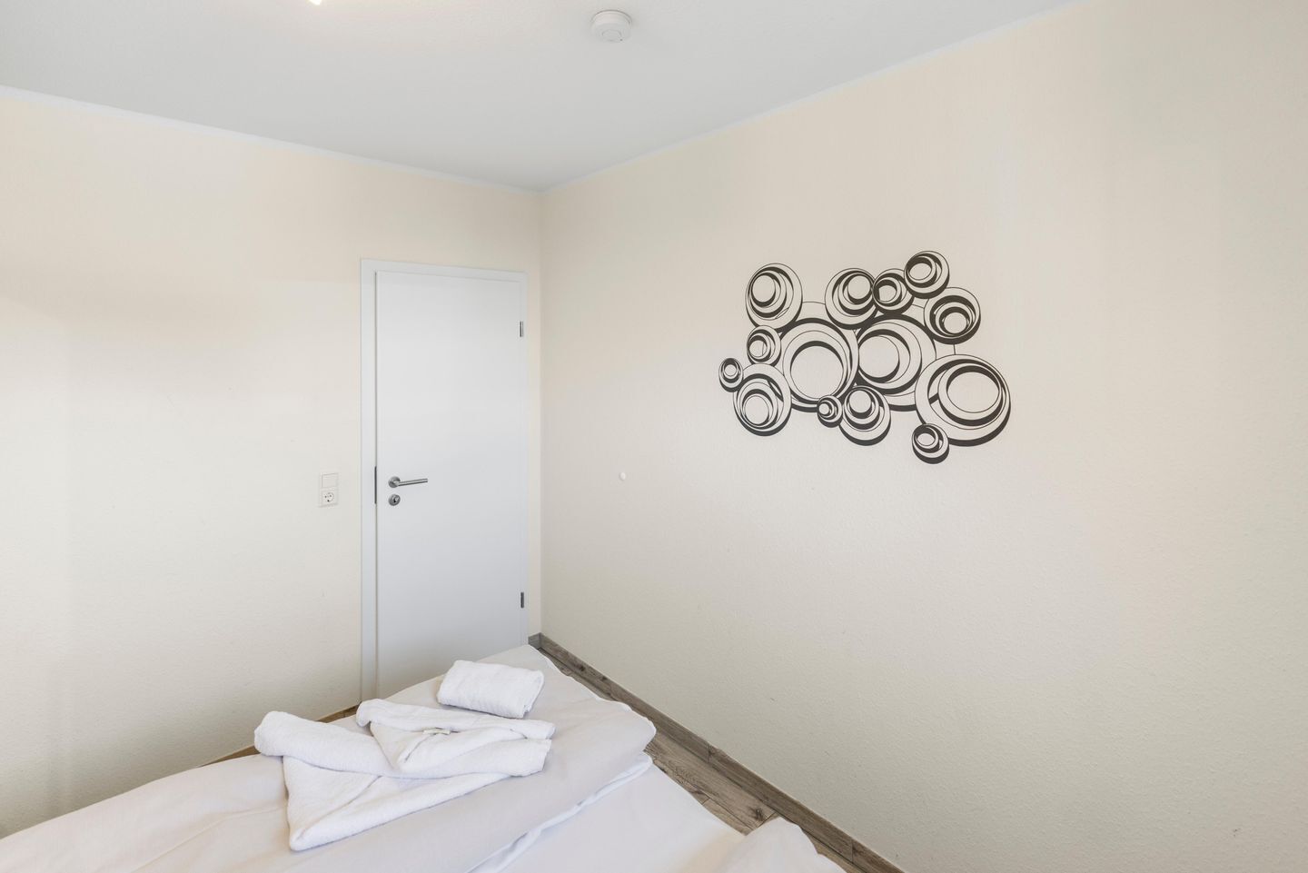 A hotel room with a bed, a white door, and a wall decoration.