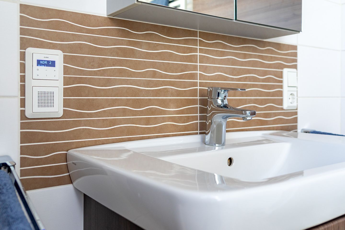 Ein Badezimmer mit Waschbecken, einer chromfarbenen Armatur und einem an der Wand montierten NDR 2 Gerät.