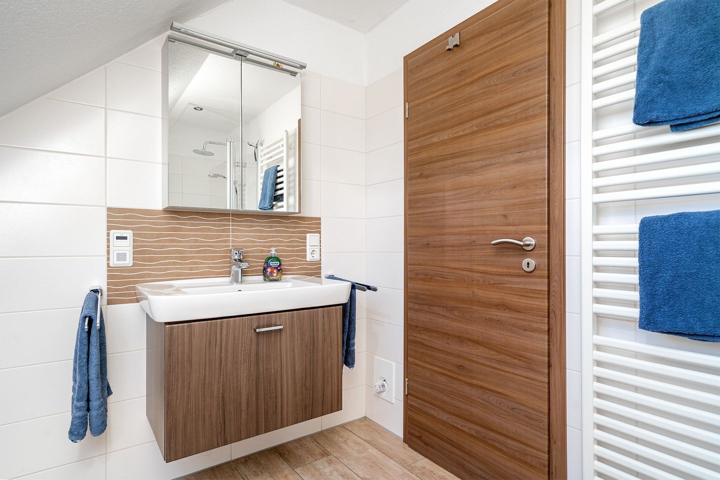 A modern bathroom with a wooden vanity, a mirror, a shower, and a towel rack.