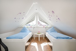 A small, triangular attic bedroom with two single beds, a small table, and a window with a view.