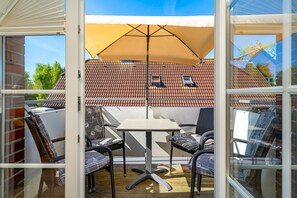 A sunlit patio with a table and chairs, a yellow umbrella, and a view of a red-tiled roof.