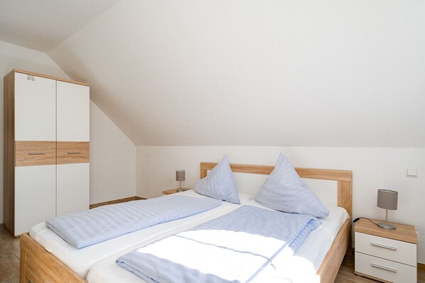 A bedroom with a bed, two bedside tables, a wardrobe, and a sloped ceiling.