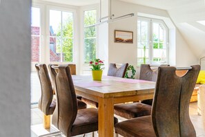 A dining area with a wooden table, brown upholstered chairs, a potted plant, and a window with a view of a brick building.