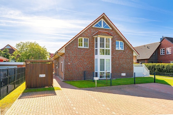 A brick house with a large central window, a small porch, and a paved driveway.