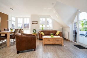 A spacious living room with a wooden coffee table, a brown sofa, and a dining area with a wooden table and chairs.
