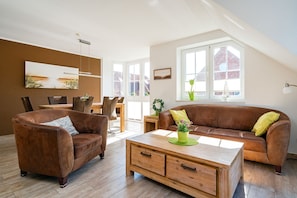 A spacious living room with a brown leather sofa, a wooden coffee table, and a dining area with a table and chairs.